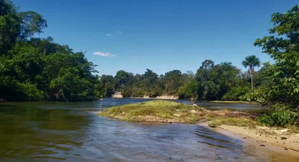 Foto de um rio escuro, com vegetação nas proximidades e uma porção de terra adentrado o corpo do rio