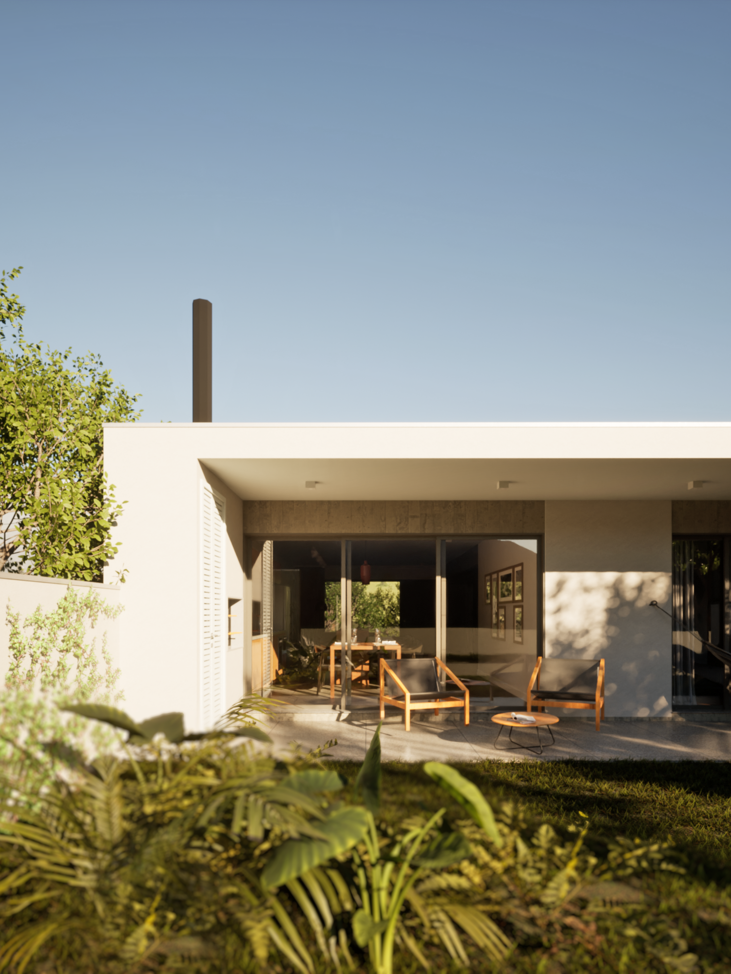 Imagem de uma varanda dos fundos da casa, com uma planta em primeiro plano. Na varanda vemos duas cadeiras tipo poltrona de madeira, com uma mesa de centro.