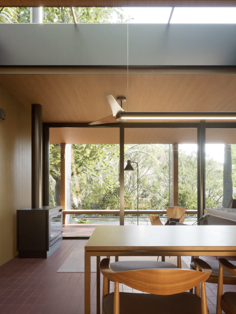 Foto de uma casa de campo, vista de dentro para fora, com mesa e cadeira de jantar em madeira no primeiro plano, e esquadria ao fundo com vista para a paisagem natural, de vegetação